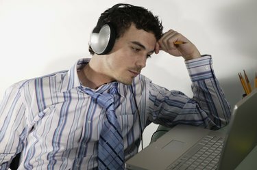 მოწყენილი ბიზნესმენი მუსიკის მოსმენისას ლეპტოპს იყენებს