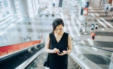 Млада пословна жена чита мејлове на паметном телефону док се вози покретним степеницама