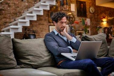 Muž pomocí přenosného počítače na gauči doma