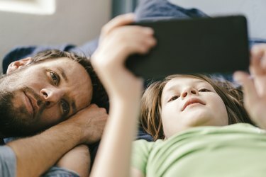 Tėvas ir sūnus kartu žiūri į išmanųjį telefoną namuose