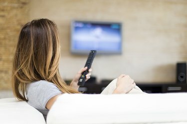 Молода жінка на дивані дивиться телевізор з плоским екраном