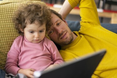 Tatăl și fiica stând întinși pe canapea uitând la un film pe tabletă