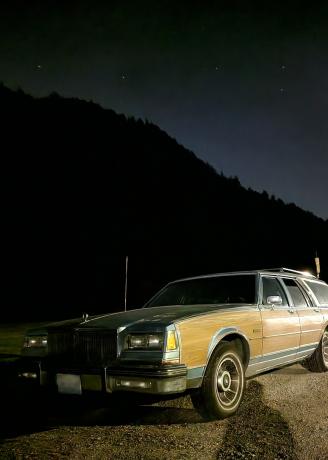 Una Buick Lesabre rivestita di pannelli di legno davanti a una montagna nera come la pece, con le stelle che brillano sullo sfondo