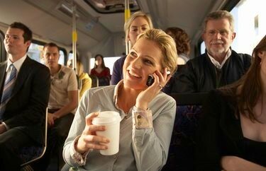 Moteris autobuse naudojasi mobiliuoju telefonu ir šypsosi