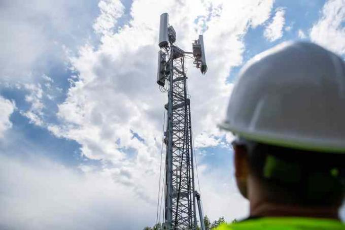 Travailleur regardant la tour 5G contre un ciel nuageux.