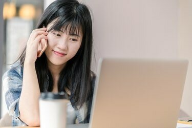 Gelukkige Aziatische student met behulp van slimme telefoon en laptop in café