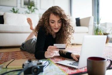 Mladá dospívající dívka s notebookem, fotoaparátem a mapou drží kartu a provádí online platby.