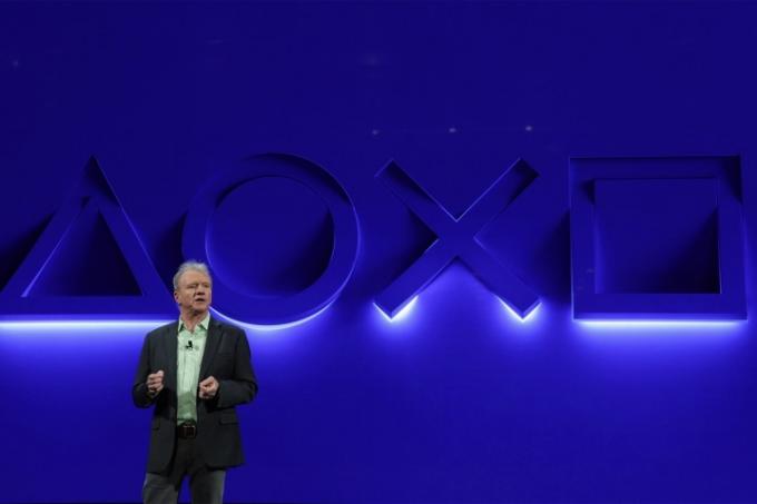 Playstationin toimitusjohtaja Jim Ryan seisoo sinisen seinän edessä Playstation-painikesymbolien valaistuna.