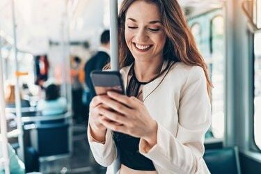 Glimlachende jonge vrouw met mobiele telefoon in de bus