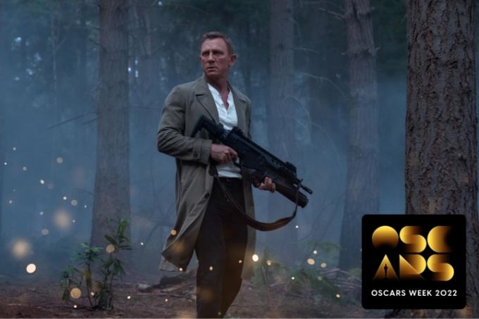 „Oskarų savaitės“ ženklelis ant Danielio Craigo atvaizdo stovi miške su šautuvu scenoje iš No Time To Die.