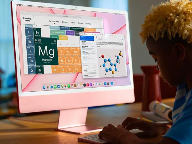 Un estudiante escribe en un escritorio en una computadora de escritorio Apple iMac M1 de 24 pulgadas de color rosa.