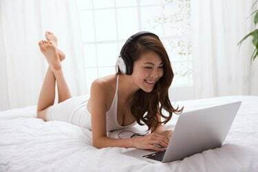 Девушка с ноутбуком и слушает музыку на кровати
