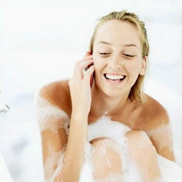 Iš arti besišypsančios ir mobiliuoju telefonu kalbančios jaunos moters vaizdas vonioje