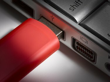 Црвени УСБ флеш чврсти диск прикључен на лаптоп, крупни план
