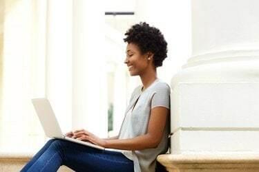 ノートパソコンを使用して外に座っている若いアフリカの女性