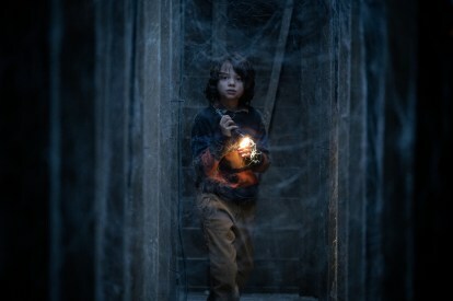 Woody Norman drži svetilko v temnem prostoru v pajčevini.