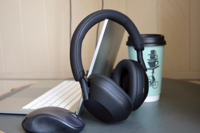 Brezžične slušalke Sony WH-1000XM5 poleg prenosnika, miške in skodelice za kavo.