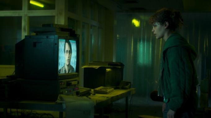Iola Evans starrt in einer Szene aus „Choose Or Die“ auf einen Fernsehbildschirm.