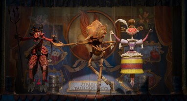 Pinocchio si inchina mentre si esibisce sul palco con diverse marionette.
