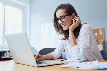 Retrato de uma bela jovem alegre empresária trabalhando em um laptop e rindo no escritório em casa