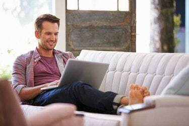 Férfi pihen a kanapén otthon laptop számítógép segítségével
