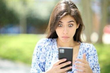 Verwirrte Frau, die auf der Straße ihr Telefon überprüft