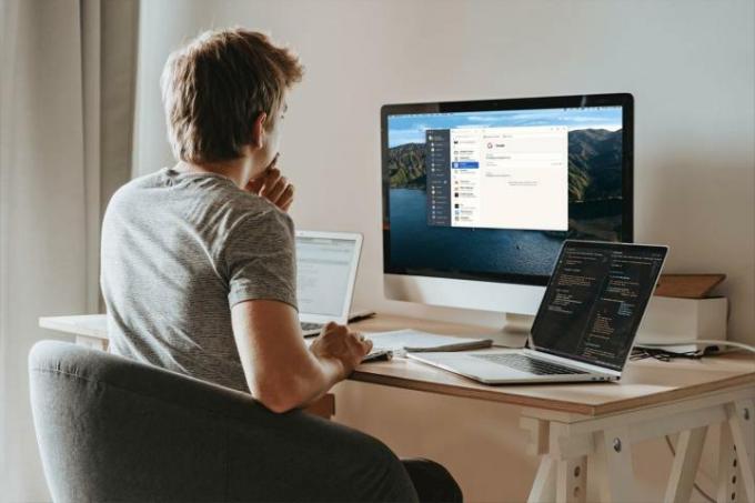 Uma pessoa usando o 1Password em um computador multifuncional de mesa enquanto está sentada em uma mesa. Há dois laptops ao lado deles na mesa.