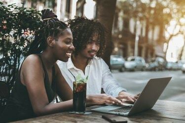 Διαφυλετικό ζευγάρι φίλων στο μπαρ σε εξωτερικούς χώρους με το netbook
