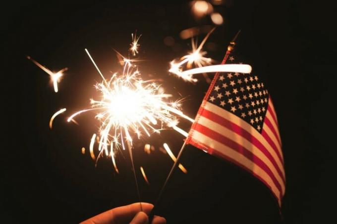O mână care ține un steag american cu un foc de artificii.