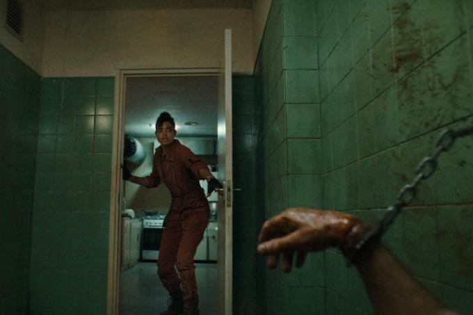 Ella Balinska sa pozrie do dverí a v scéne zo série Resident Evil na Netflixe vidí krvavú, spútanú ruku.