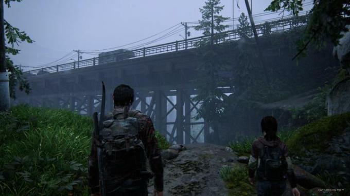 Joel ve Ellie, The Last of Us Part I'de bir köprüye bakıyor.