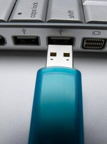 Unidad flash USB turquesa a punto de conectarse a la computadora portátil, primer plano