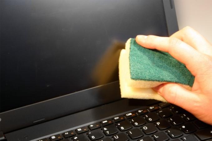 Рука человека чистит экран ноутбука губкой.