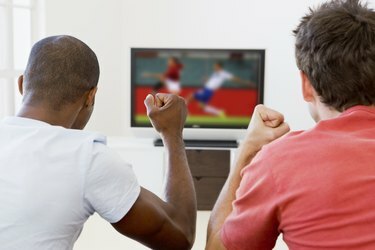 Два мушкарца у дневној соби гледају телевизију и навијају