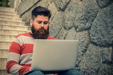 Nuori hipsteri istuu ja käyttää kannettavaa tietokonetta