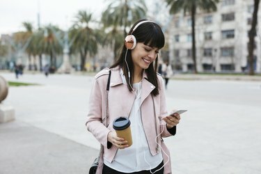 Spānija, Barselona, ​​smaidoša sieviete ar kafiju, mobilais tālrunis un austiņas pilsētā