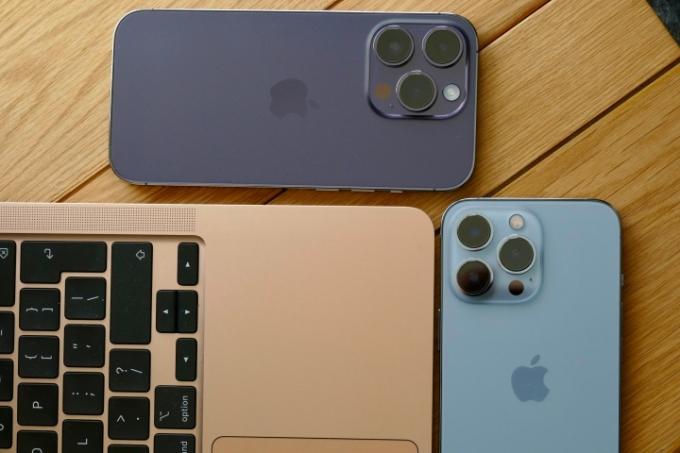 iPhone 14 Pro a iPhone 13 Pro lícem dolů na stole s MacBookem Air.