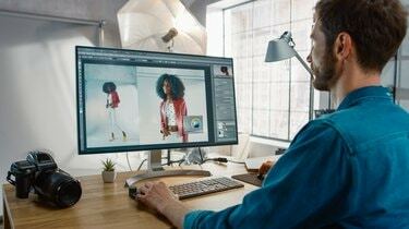 Professionell fotograf som sitter vid sitt skrivbord använder stationär dator i en fotostudio retuscherar. Efter fotograferingen retuscherar han fotografier av vacker svart kvinnlig modell i ett bildredigeringsprogram