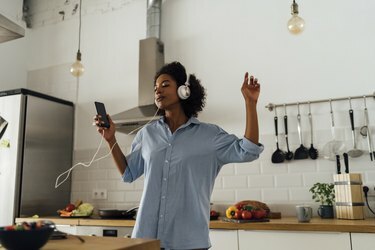 Kvinde danser og lytter til musik om morgenen i sit køkken