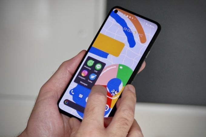 Kāds tur Google Pixel 5. Ekrāns ir ieslēgts un parāda sākuma ekrānu ar atvērtu lietotņu mapi.