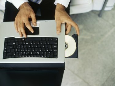 Aukšto kampo vaizdas, kuriame verslininkas įdeda kompaktinį diską į nešiojamąjį kompiuterį