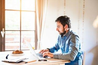Moški sedi za mizo in dela od doma na prenosnem računalniku
