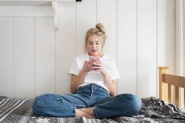Dospívající dívka s telefonem sedí na posteli