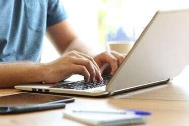 Adam bir masanın üzerinde bir dizüstü bilgisayar klavyesinde yazarak eller