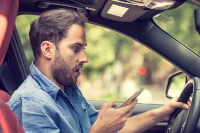 francja wysyła SMS-y podczas jazdy mężczyzna siedzi w samochodzie z ręką na telefonie komórkowym