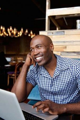 ბედნიერი აფრიკელი კაცი ლეპტოპთან ერთად კაფეში ზის