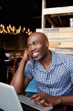 Glad afrikansk mann sitter på en kafé med laptop