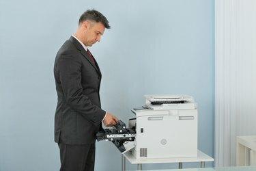 Uzņēmējs fiksē kasetni printera mašīnā birojā