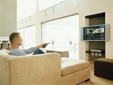परिपक्व आदमी एक आधुनिक घर के इंटीरियर में टीवी देख रहा है