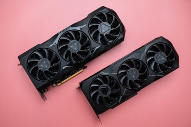 Pembe bir yüzey üzerinde iki AMD Radeon RX 7000 grafik kartı.